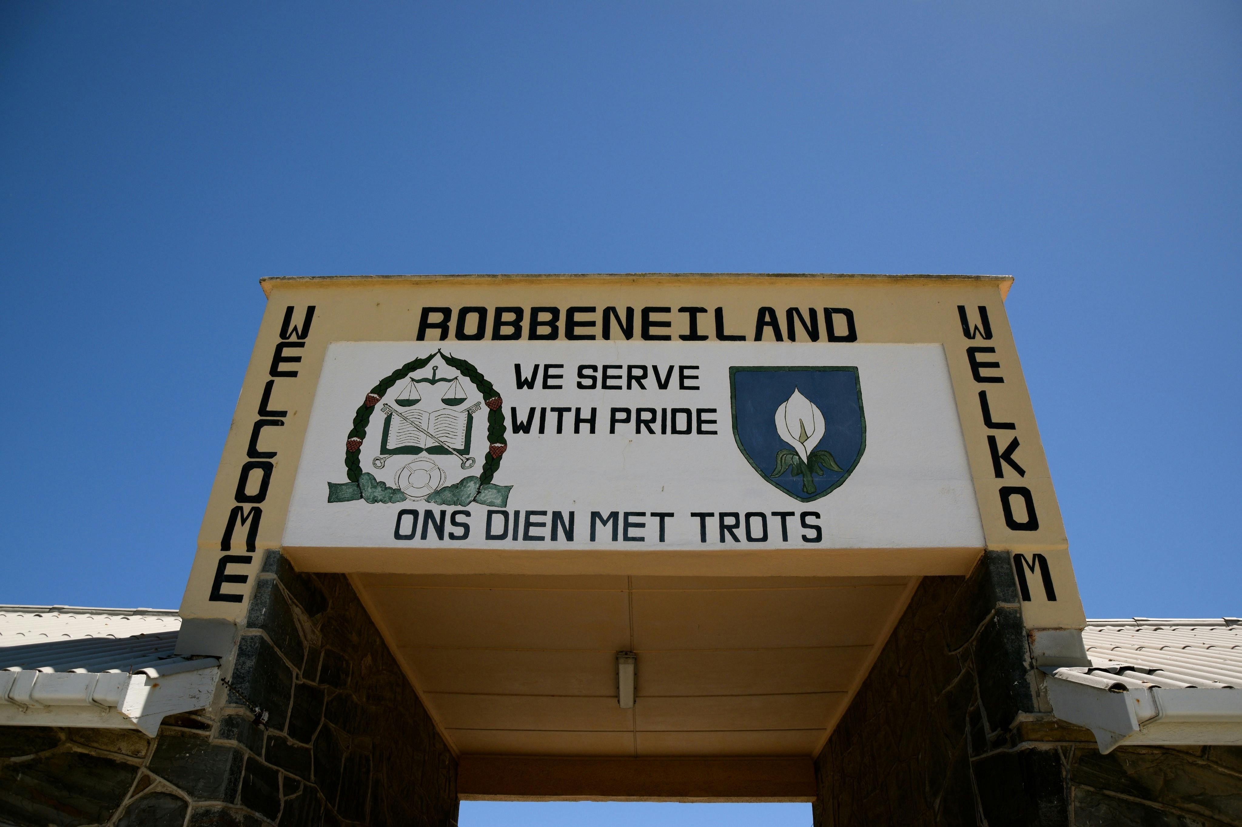 Vstupní cedule na ostrov Robben s nápisy „SLOUŽÍME S HRDOSTÍ“ a „ONS DIEN MET TROTS“ v angličtině i afrikánštině.