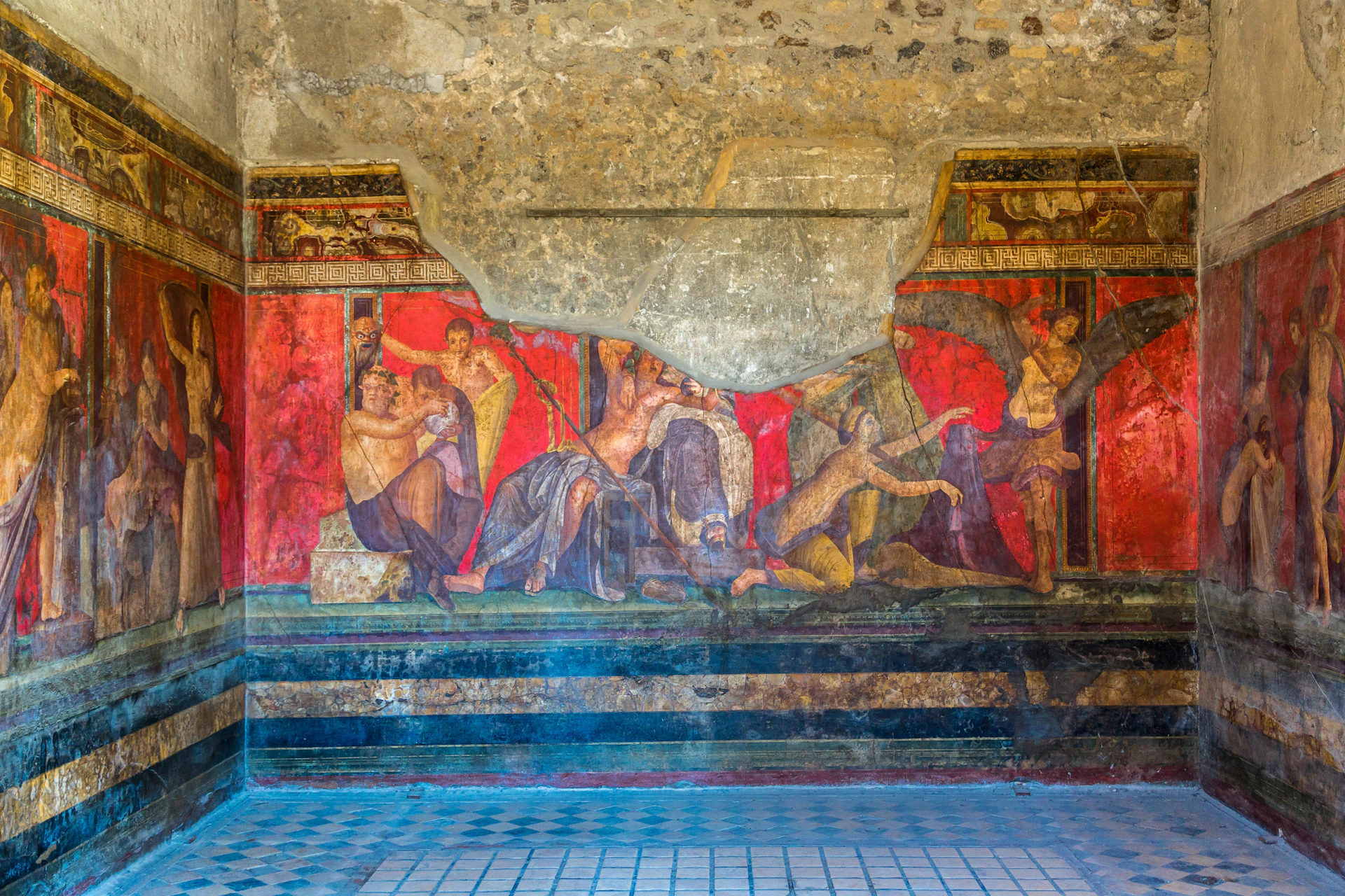Ancient fresco with red background, depicting people in various poses, partially damaged, in a room with tiled floor.