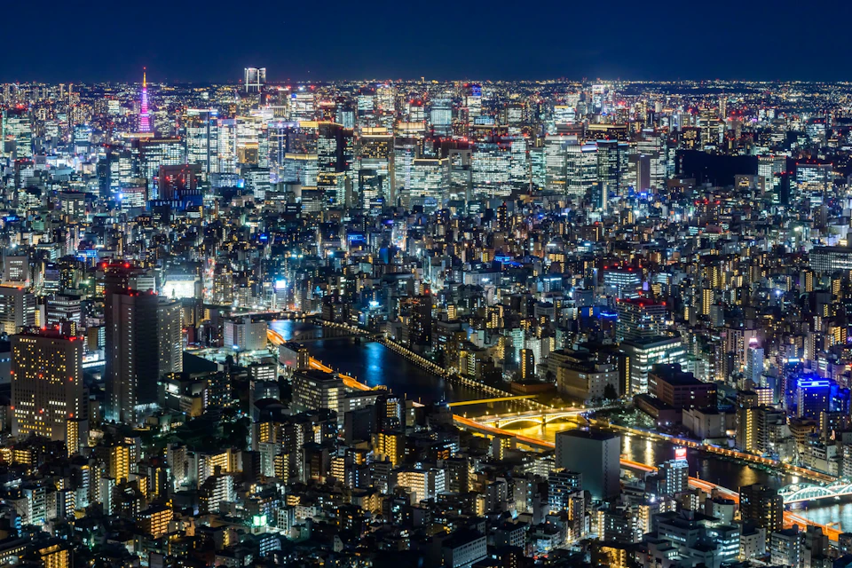 A vibrant cityscape at night with illuminated buildings, a river, and bridges under a dark sky.