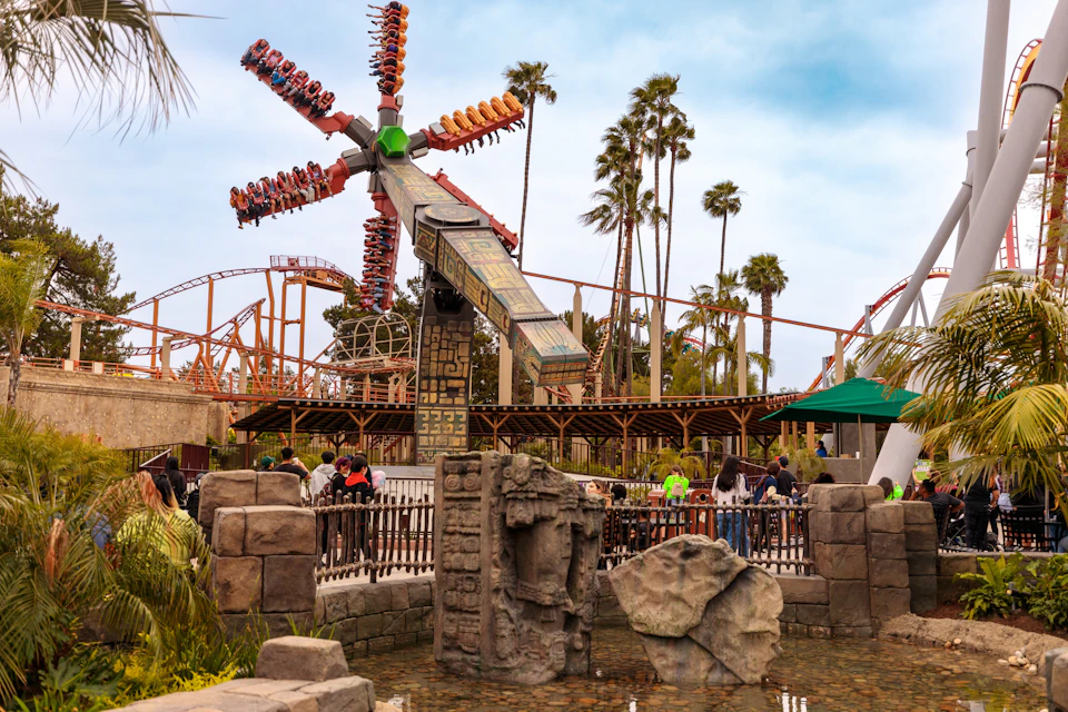 Amusement park scene with a spinning ride, roller coaster tracks in the background, and decorative stone sculptures in the foreground.