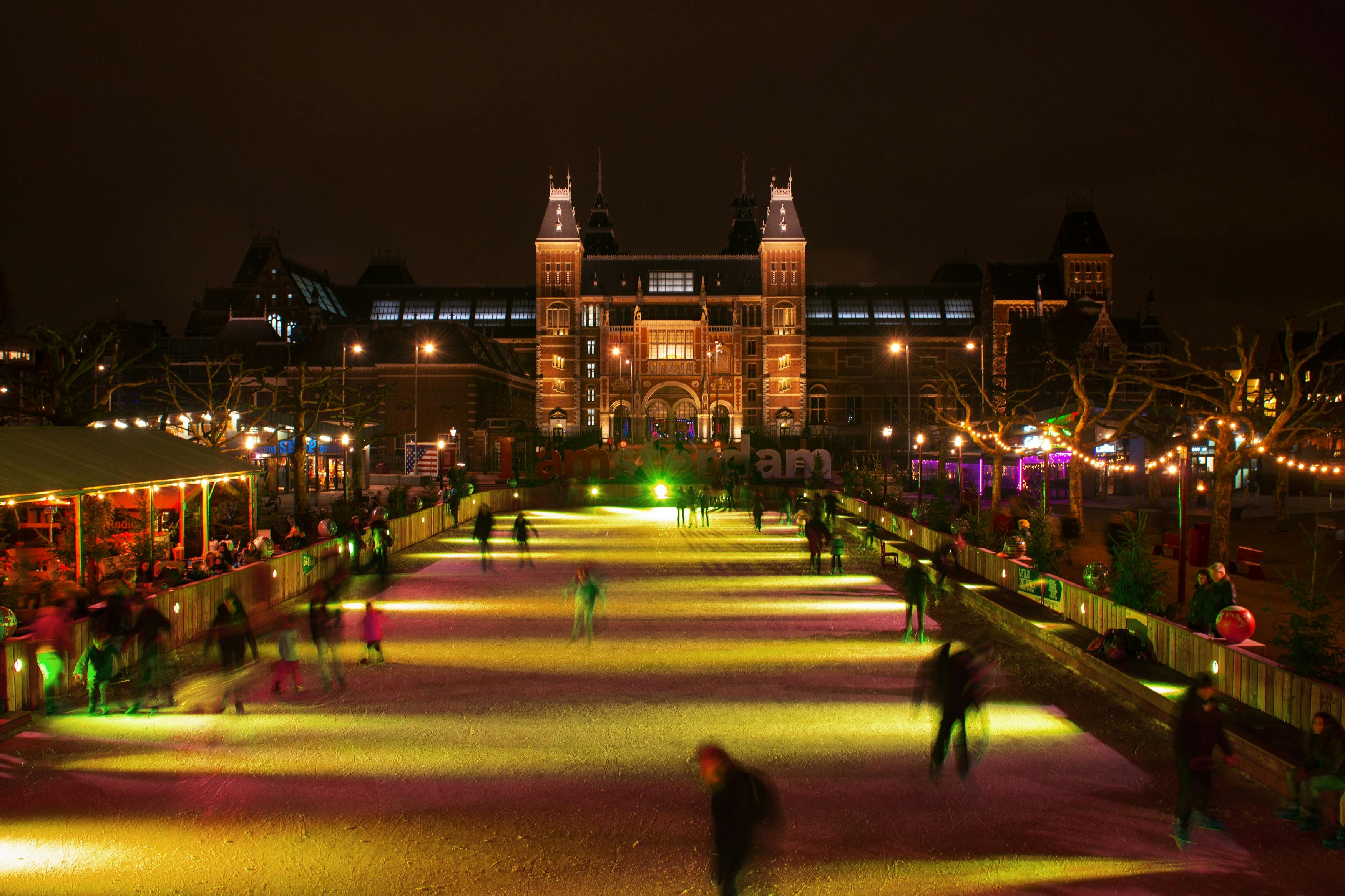 People skating on an illuminated ice rink at night, with a lit historic building in the background.