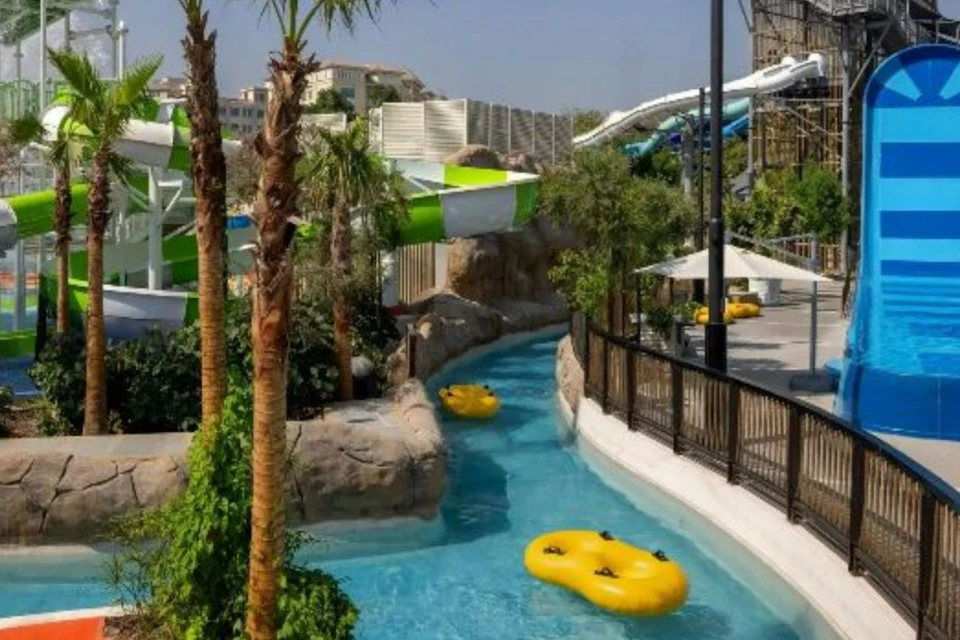 A lazy river with yellow inflatable rafts surrounded by greenery and water park structures on a sunny day.