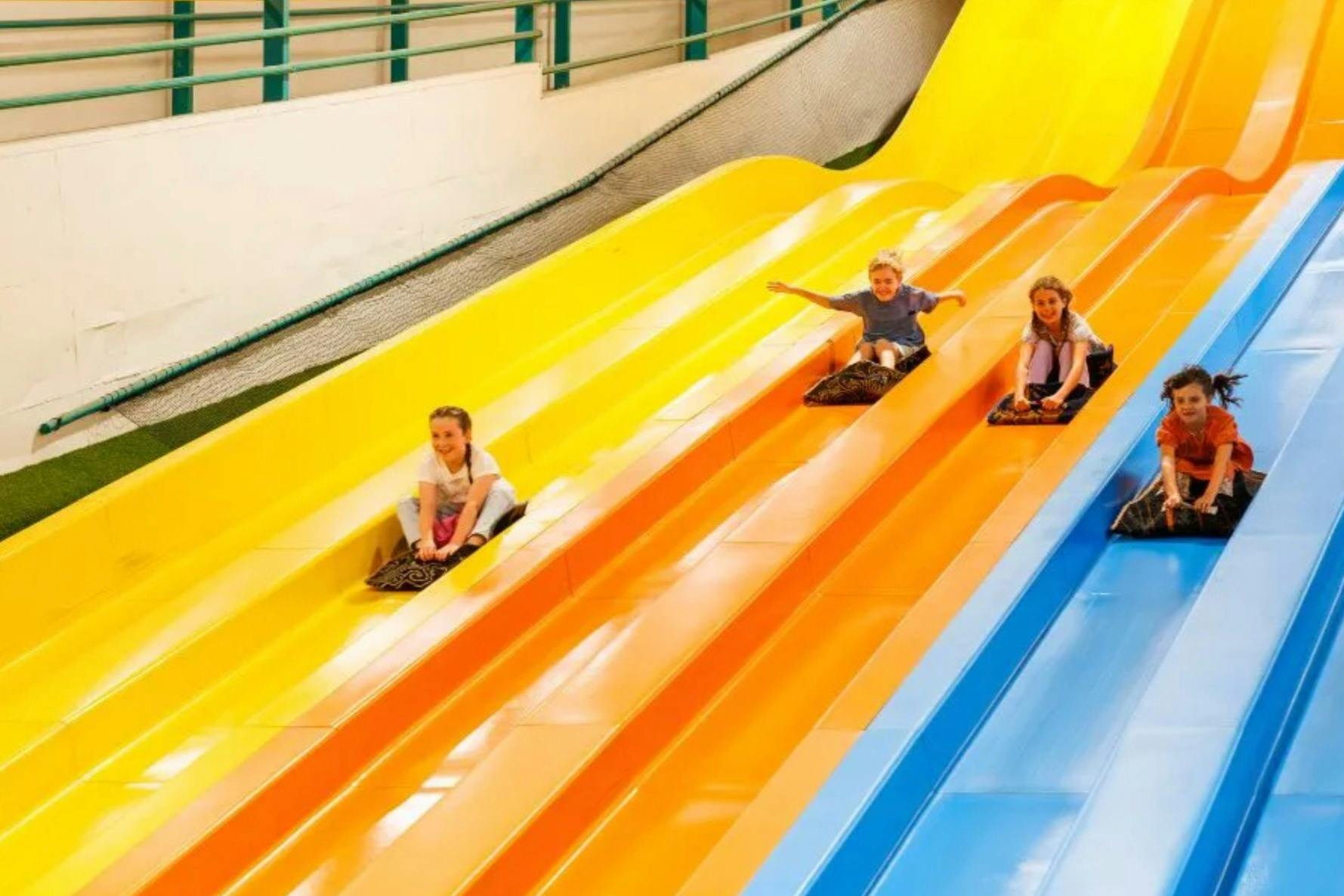 Children sliding down colorful parallel slides in an indoor playground.