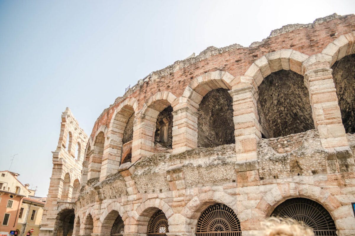 Ancient Roman amphitheater with arched stone and brickwork, partially eroded, under a clear sky.
