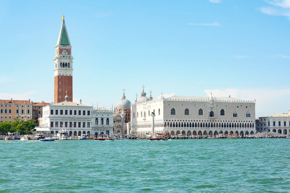 A view of the Doge's Palace and St. Mark's Campanile in Venice from across the water under a clear blue sky.