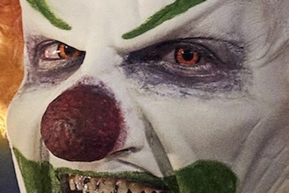 Person in a clown costume with face paint, posing at night in front of the "Welcome to Fabulous Las Vegas Nevada" sign.