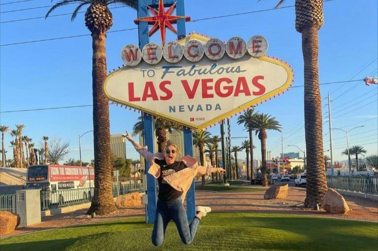 A person jumps joyfully in front of the "Welcome to Fabulous Las Vegas, Nevada" sign surrounded by palm trees.