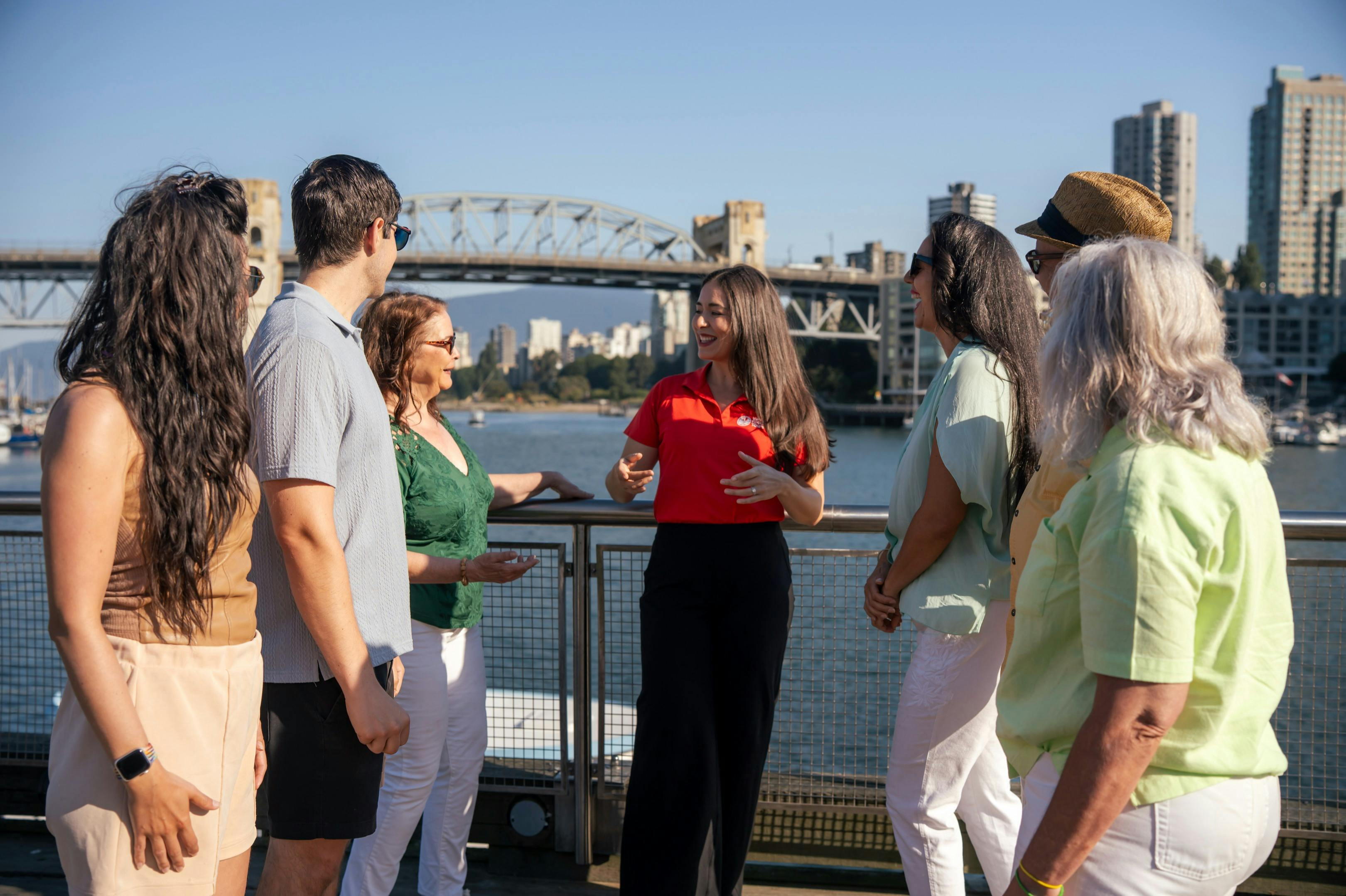 화창한 날 다리와 도시 풍경을 배경으로 난간 근처에서 다섯 명이 이야기를 나누고 있습니다.
