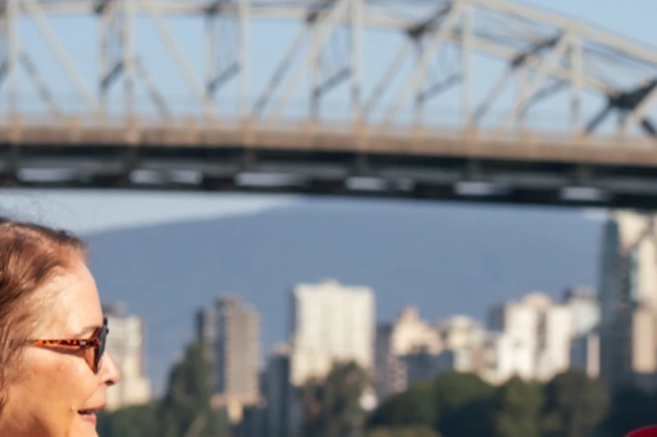 Five people talking near a railing with a bridge and cityscape in the background on a sunny day.
