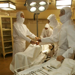 Medicinskt team i vita skyddsdräkter som utför operation under ljusa operationslampor med medicinska instrument i närheten.