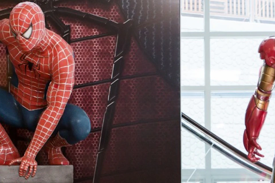 Two people posing playfully with Spider-Man and Iron Man statues in a bright indoor setting.