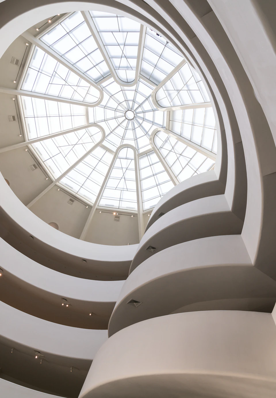 Curved balconies in a modern building beneath a large, circular glass skylight with geometric patterns.