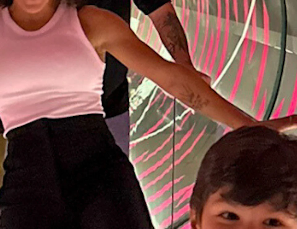 Three people walking through a spinning tunnel with pink and white stripes, holding onto railings for balance.