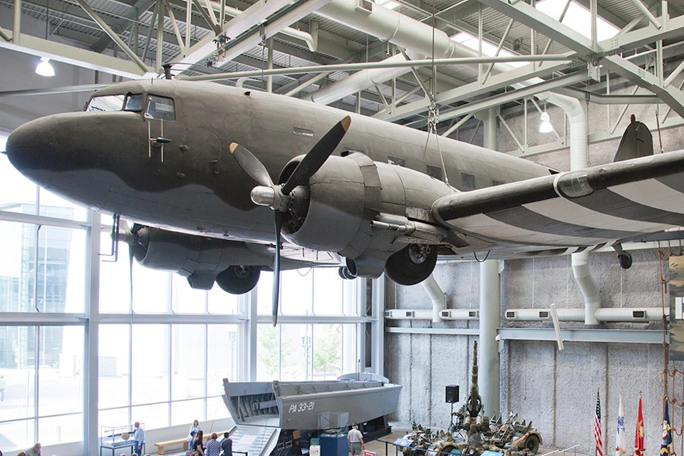 A large military aircraft suspended inside a museum, with exhibits and visitors visible below.
