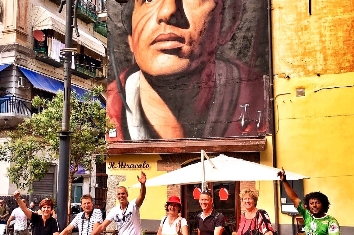 一群多元化的人在城市街道上一幅加冕男子的大型壁画下骑着自行车摆姿势。