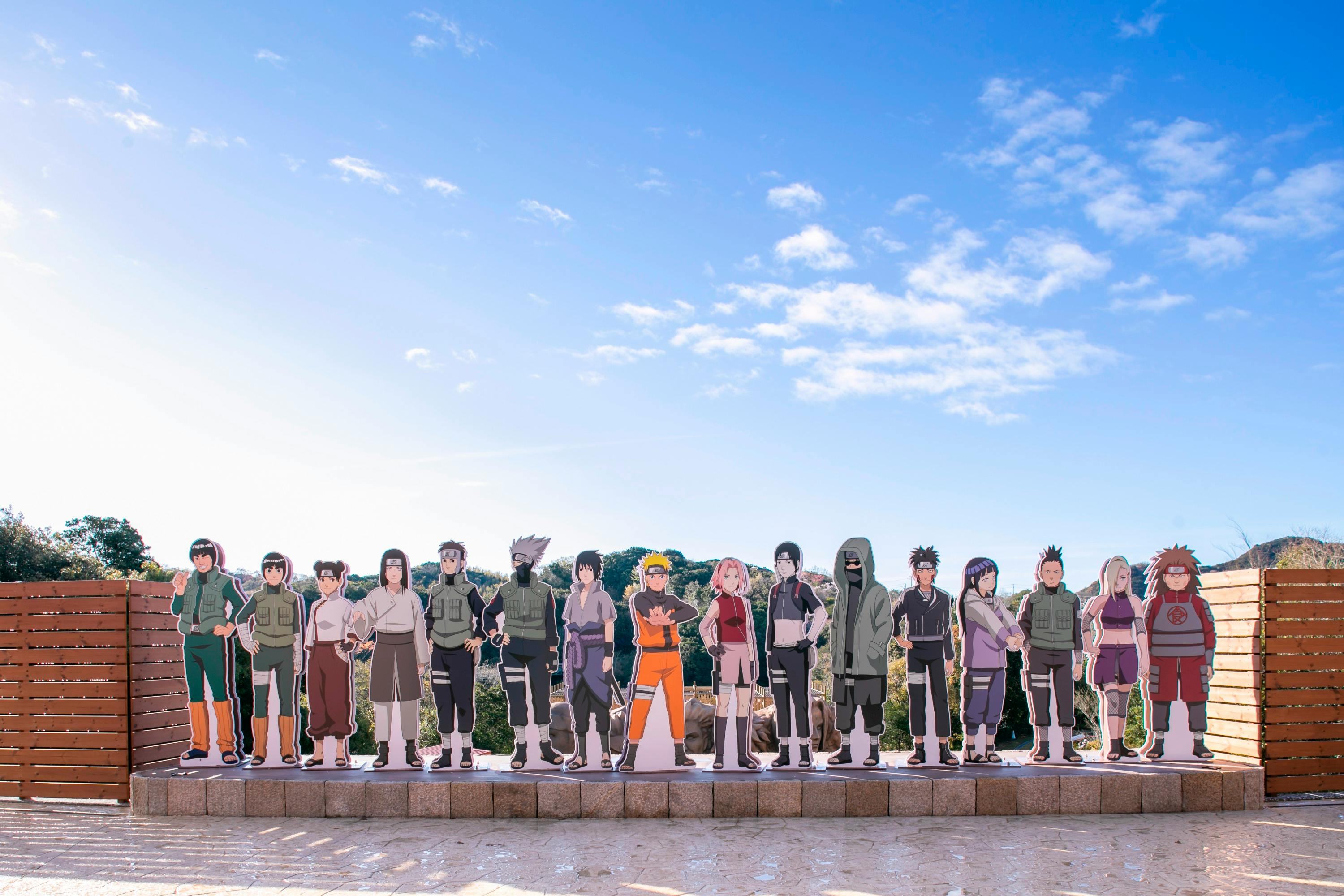 Cardboard cutouts of anime characters displayed outdoors under a clear blue sky.