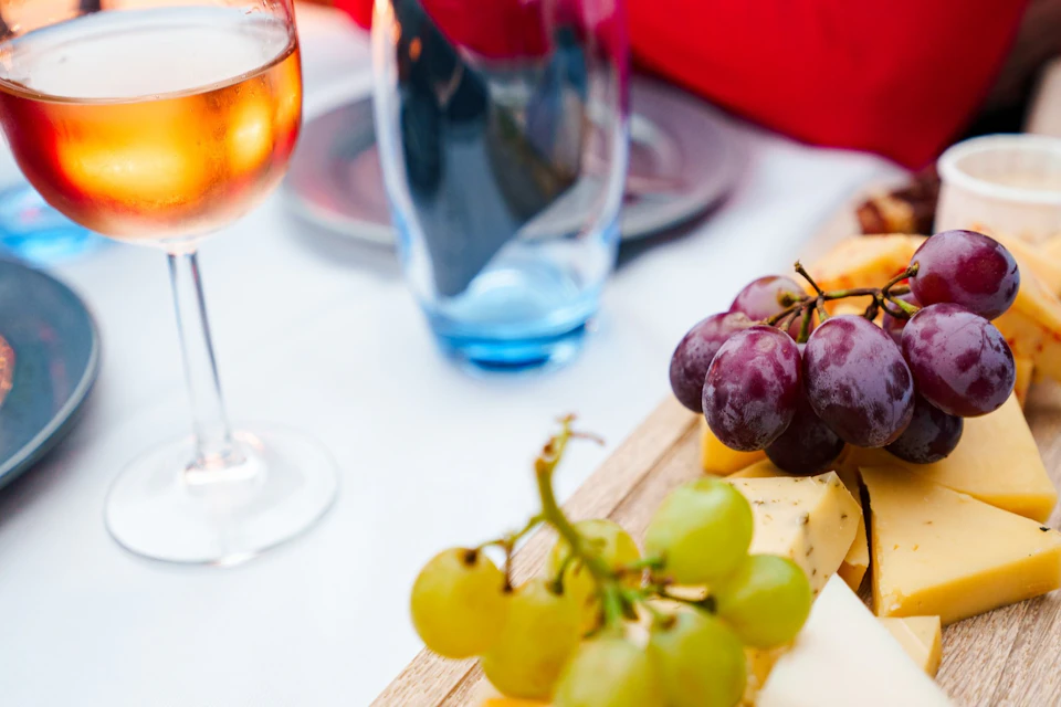 A close-up of a table setting with a glass of wine, a blue glass, and a cheese platter with grapes in focus.