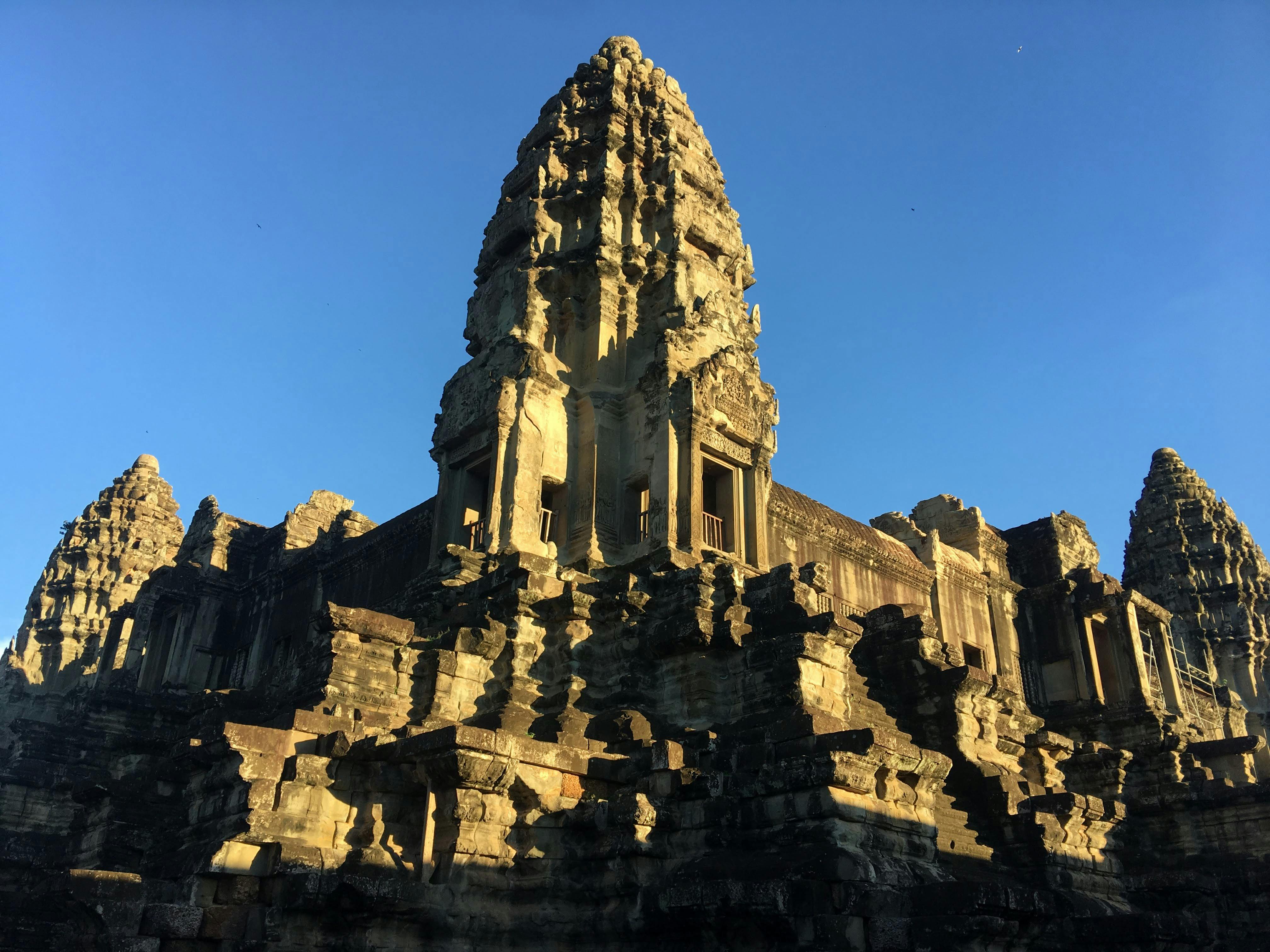 Ancient stone temple with intricate carvings, set against a clear blue sky. The structures are weathered and detailed.