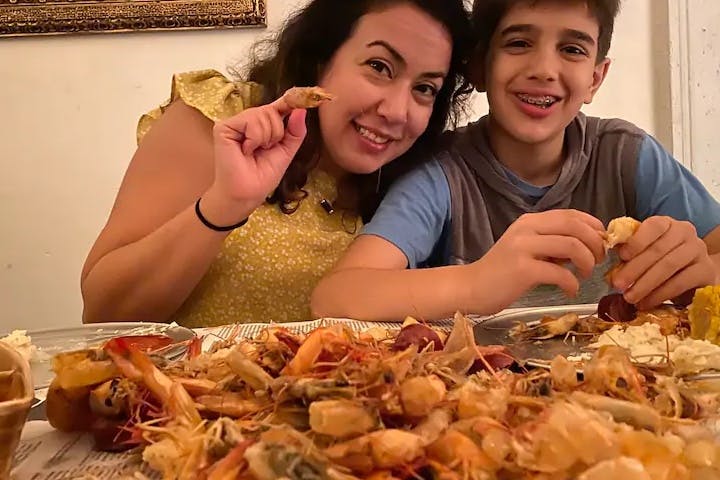 En kvinna och en pojke ler medan de skalar och äter räkor vid ett bord täckt med skaldjur.