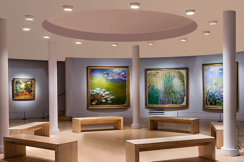 An art gallery with paintings of water lilies and benches under a circular ceiling with spotlights.