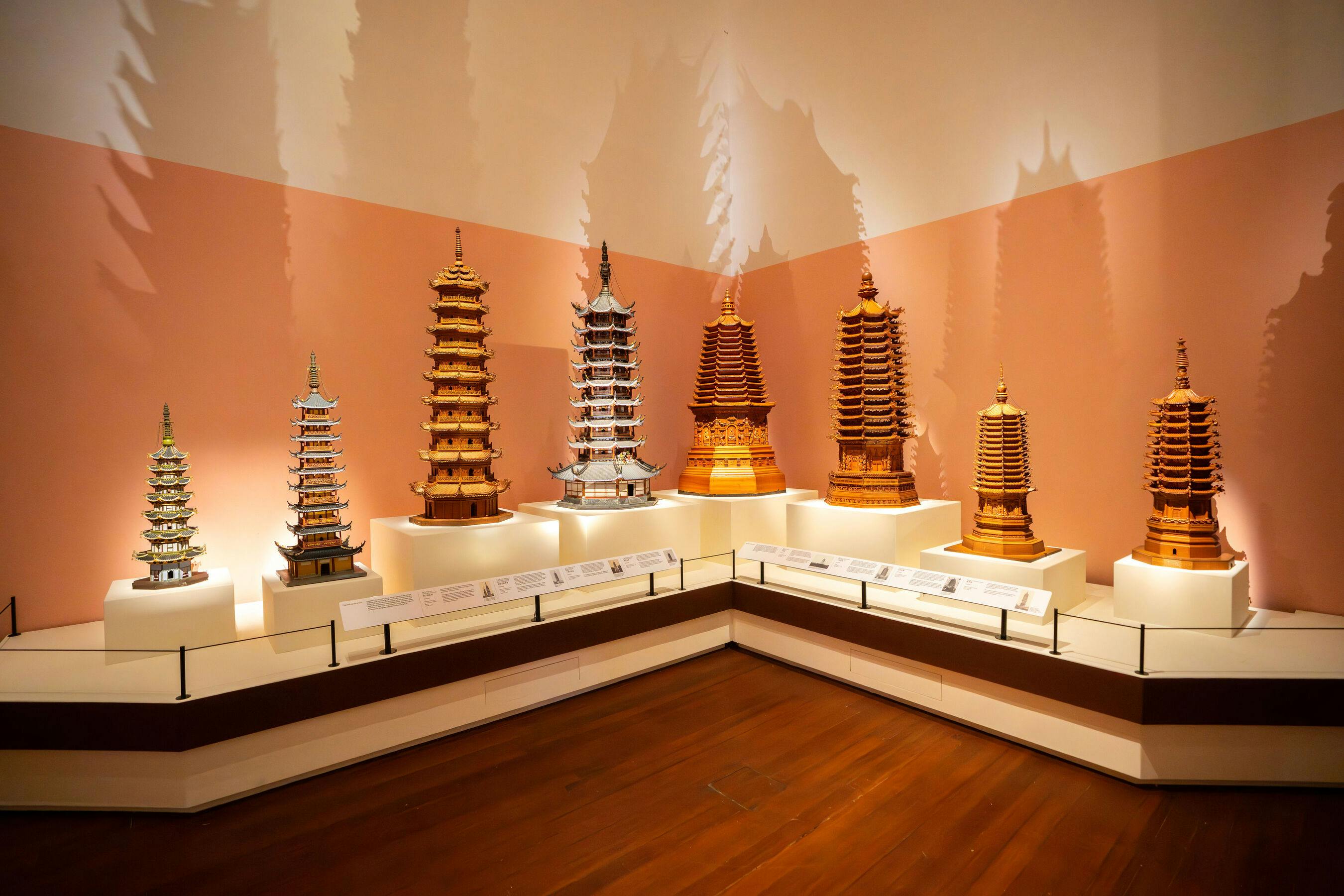 A museum display of miniature pagoda models arranged on a corner platform with informational plaques below each.