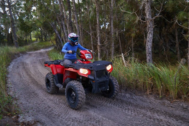 빽빽한 숲 속 흙길에서 빨간색 ATV를 타고 헬멧과 파란색 긴팔 셔츠를 입은 사람.