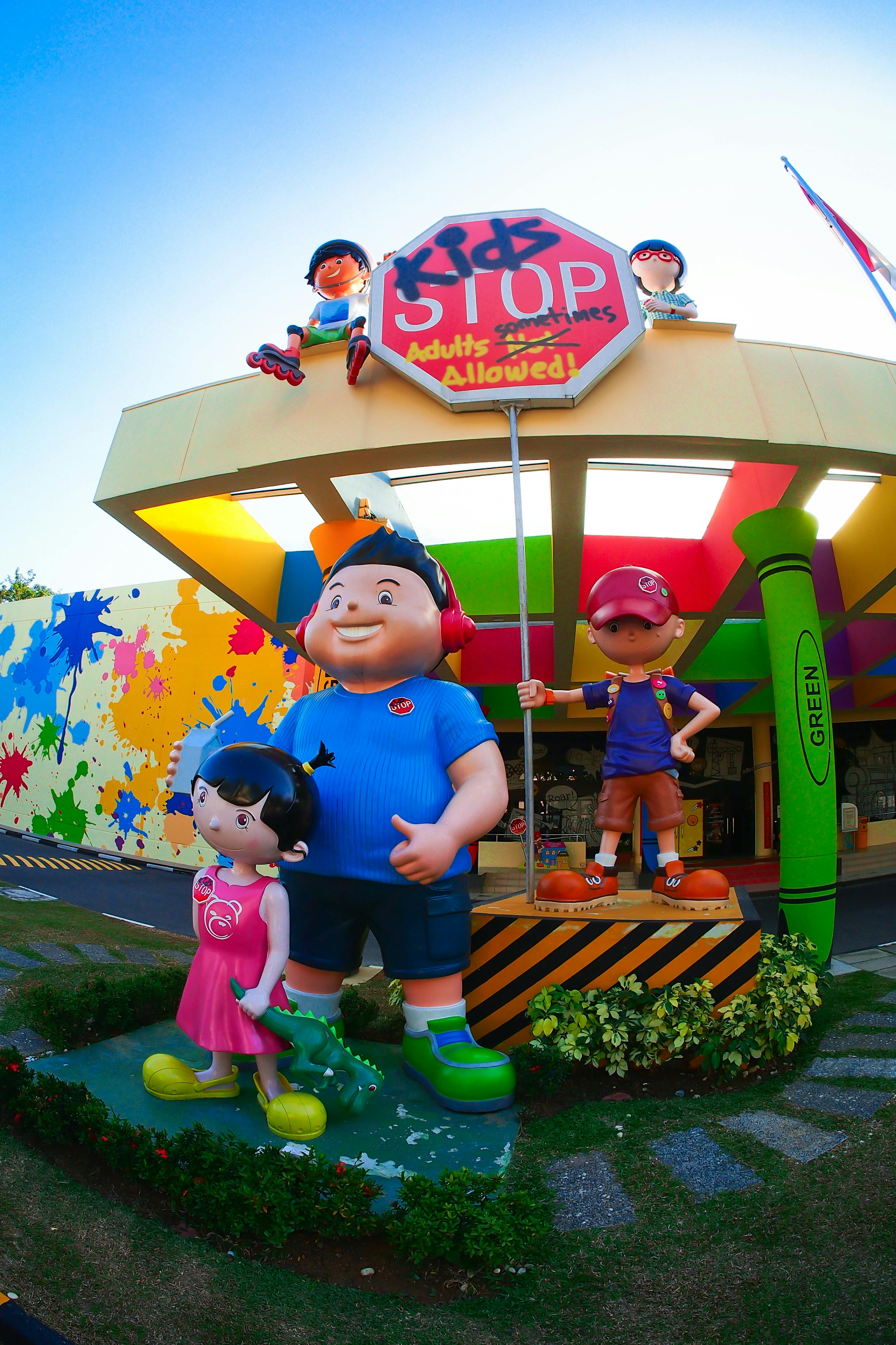 Velké, barevné sochy dětí před „Kids Stop“ s graffiti, které je zdůrazňují jako vstup vhodný pro děti.