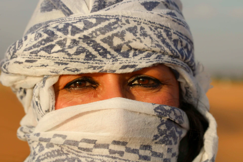 Close-up of a person's face with deep brown eyes, partially covered by a patterned white and blue cloth.