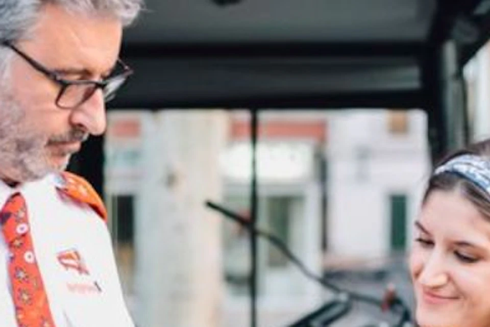 Bus driver checking a young woman's phone at the bus entrance. The driver holds a blue pen and wears glasses and a uniform.