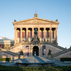 En neoklassisk byggnad med stora trappor, pelare och statyer. Banderoller flankerar ingången, och en skulptur sitter ovanpå trappan.