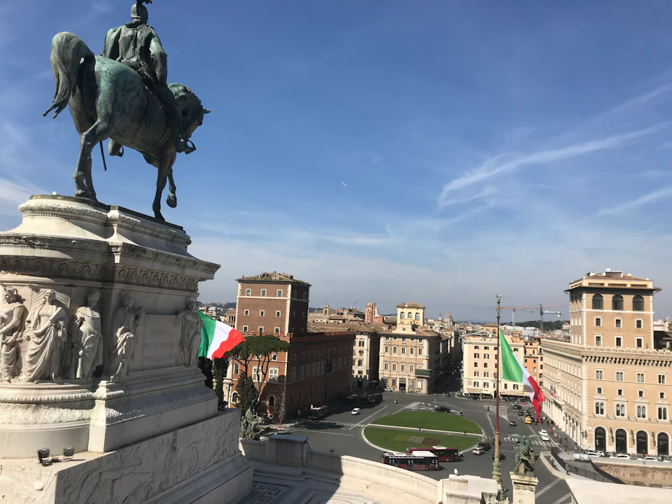 Equestrian statue with Italian flags, overlooking a city square with historic buildings under a clear blue sky.