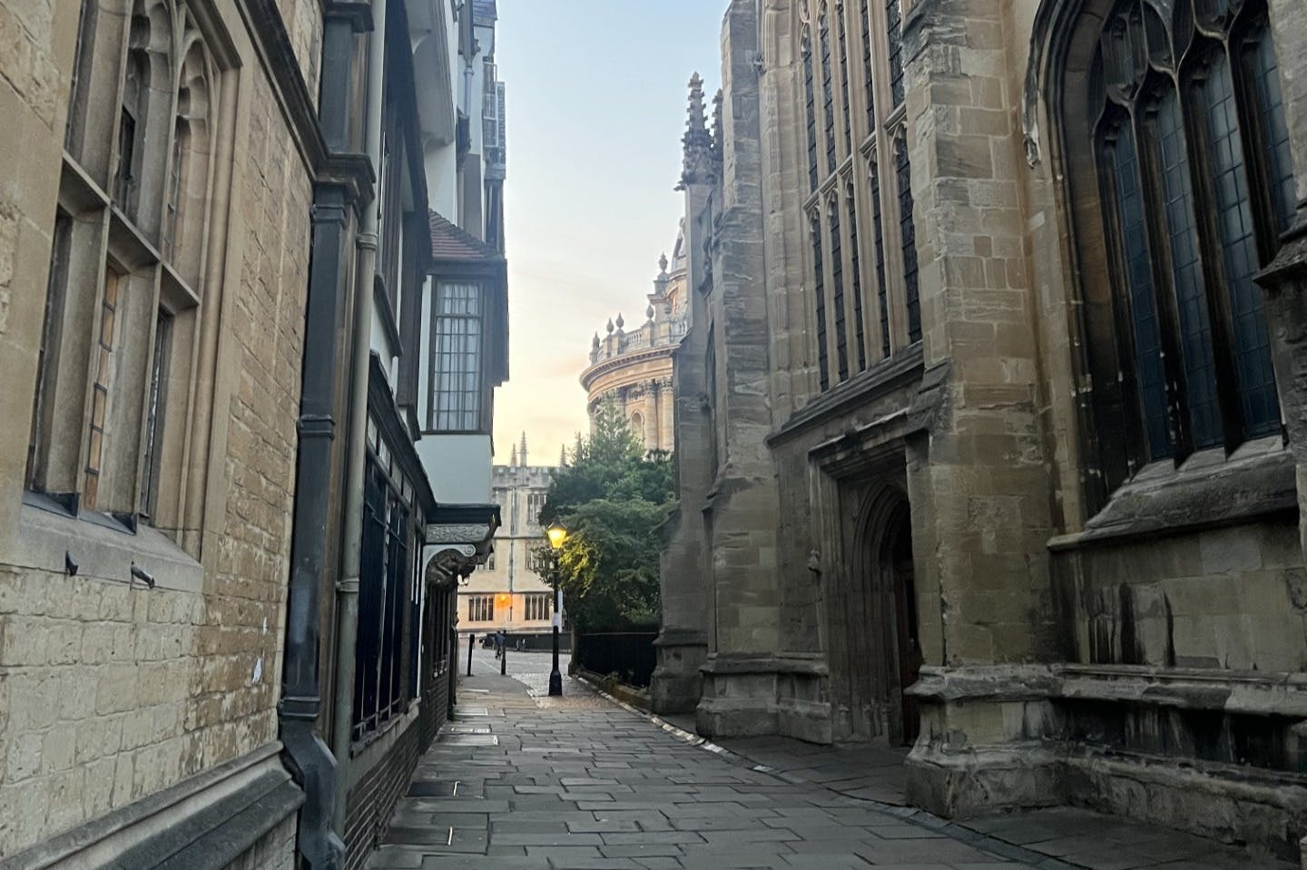 A narrow stone-paved alley between historical buildings leads to a circular structure with ornate details in the background.