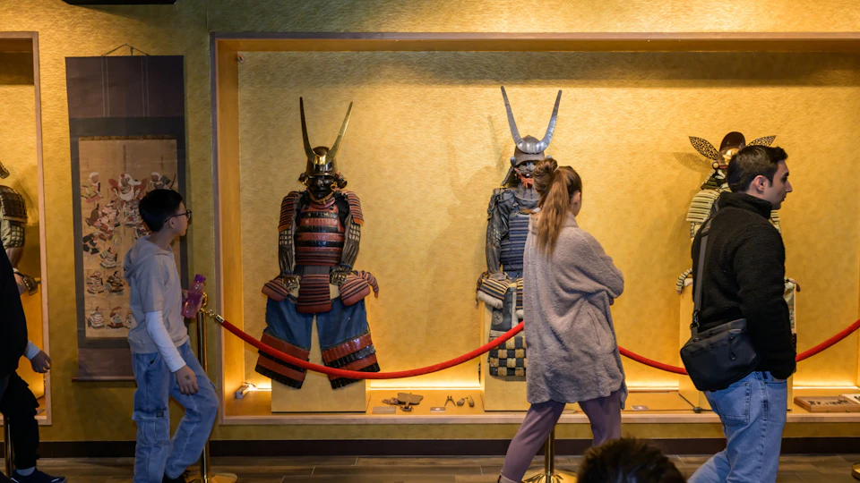Two sets of traditional samurai armor displayed in a museum exhibit, with a person walking past in the foreground.