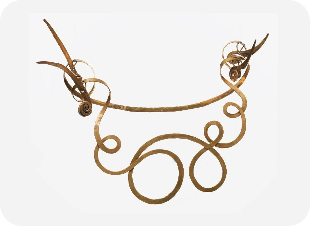 An artistic gold necklace with intricate swirls and loops, featuring a delicate and ornate design against a white background.