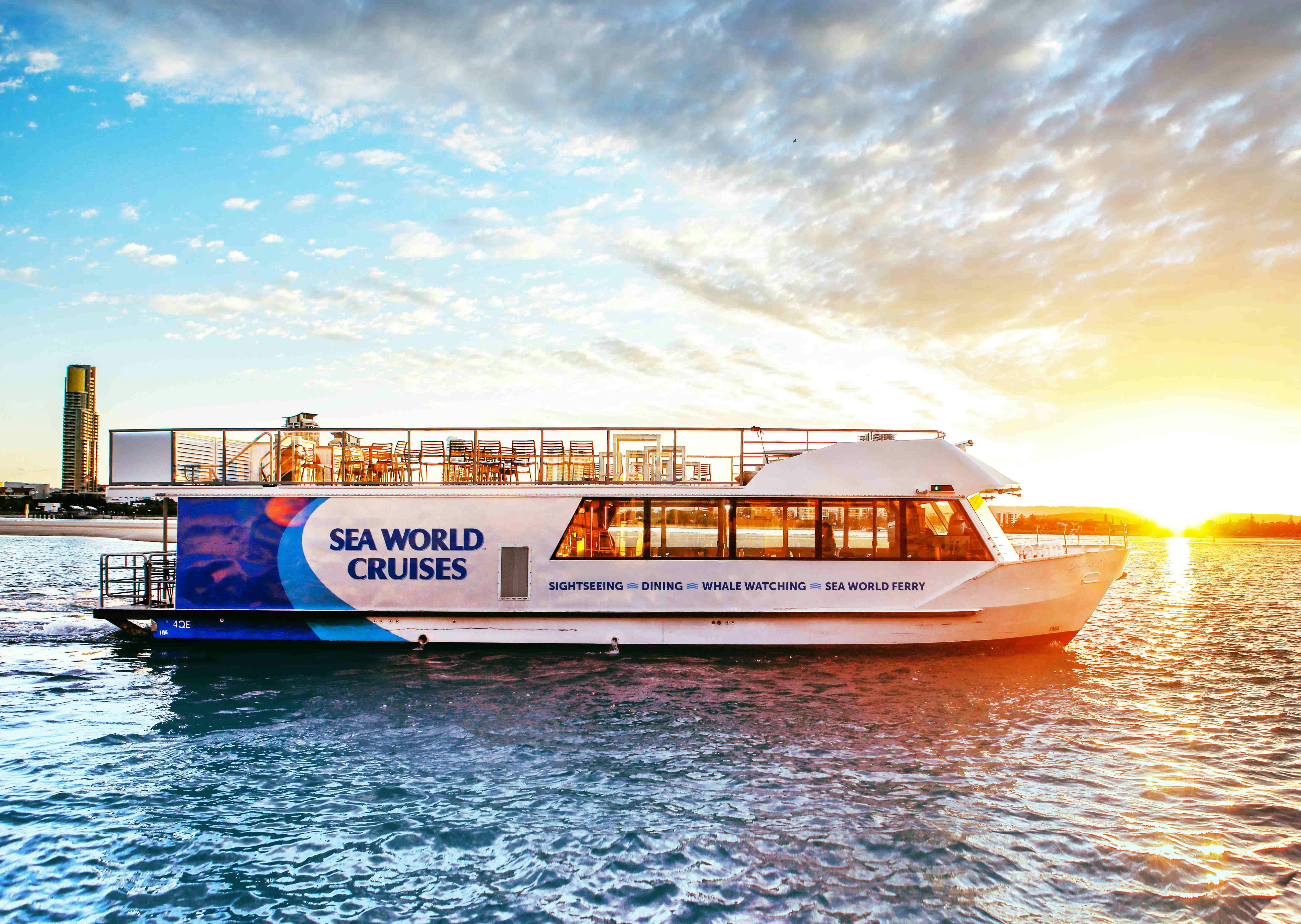 日落时分，在一片多云的天空下，一艘标有“海洋世界游轮”的渡轮在水上航行。