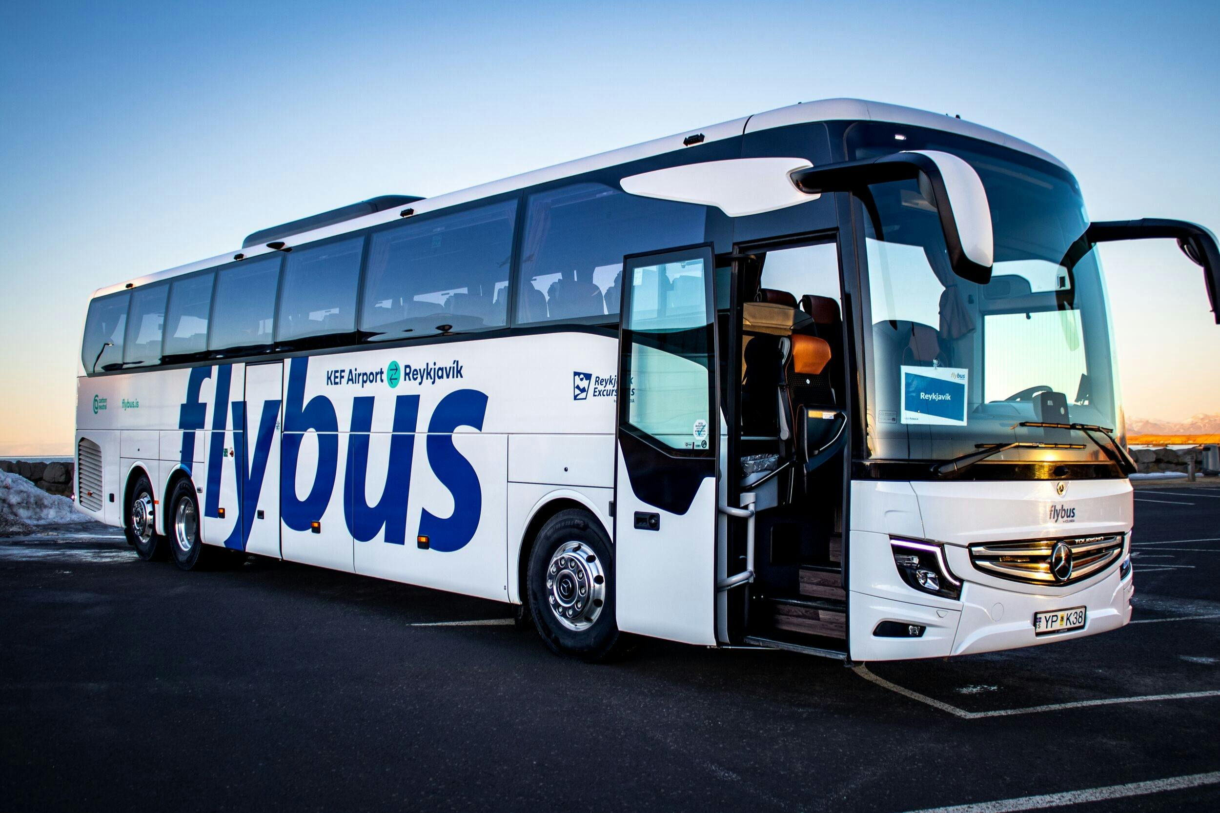 Белый автобус с надписью «Flybus» припаркован с открытой дверью на фоне ясного неба.