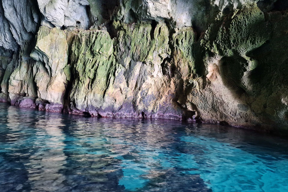 Rocky cave walls covered in green moss with clear blue water at the base.