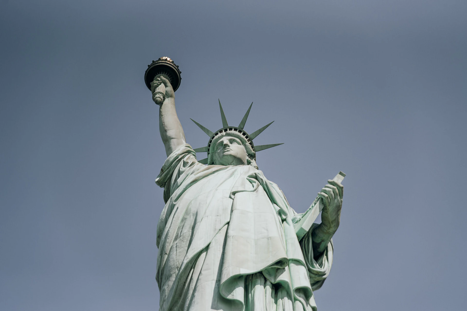 The Statue of Liberty holding a torch in her raised right hand and a tablet in her left hand, against a clear sky.