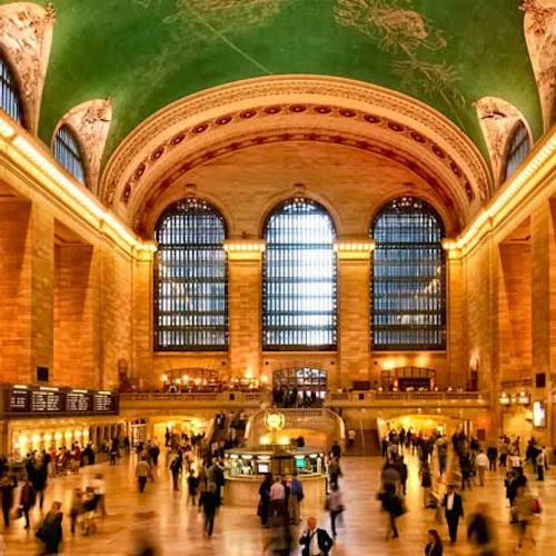 Das überfüllte Grand Central Terminal mit seinen hohen Bogenfenstern, der grünen, verzierten Decke, der großen amerikanischen Flagge und den geschäftigen Reisenden.