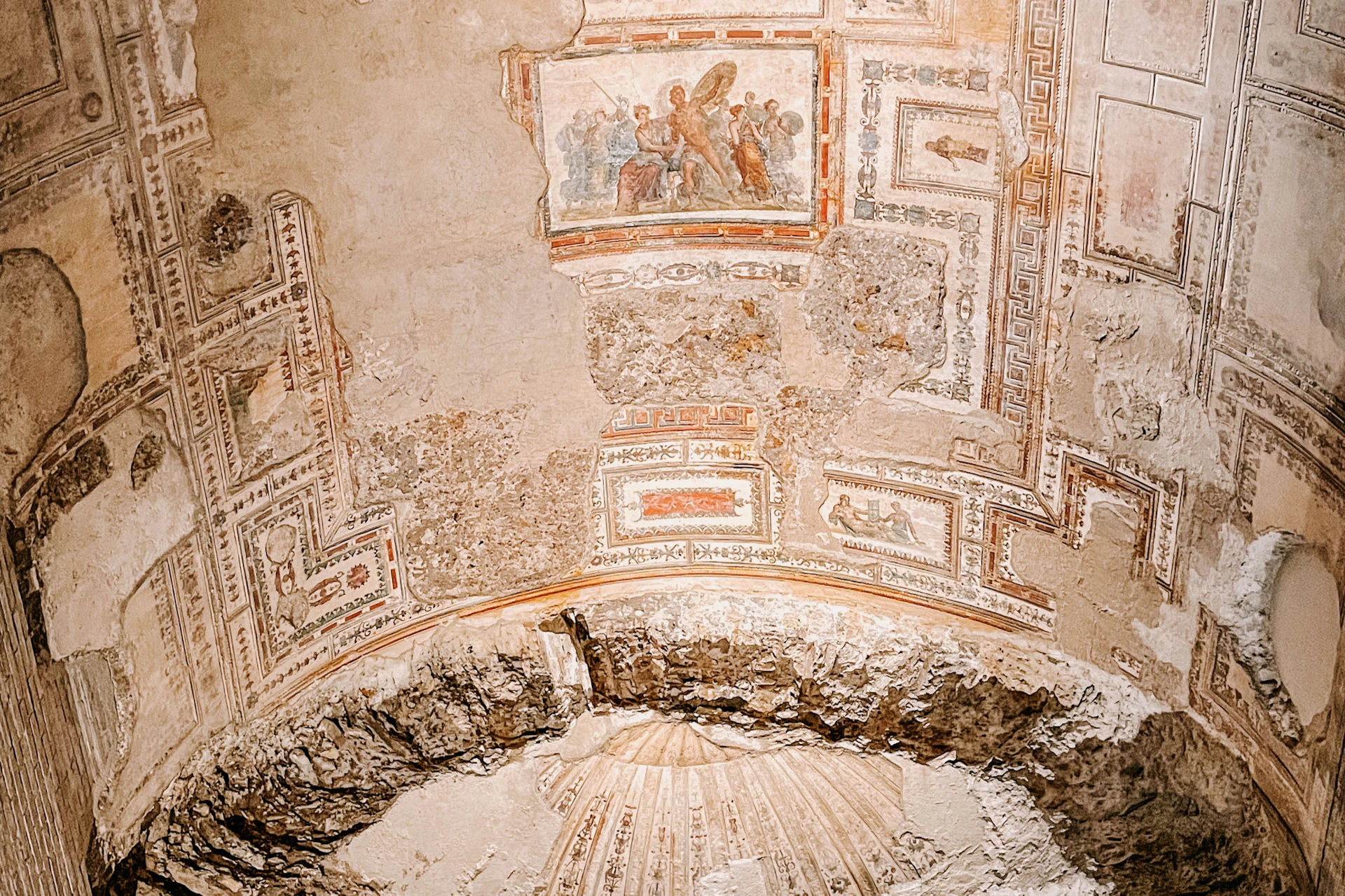 A frescoed wall with classical-style artwork and decorative patterns, part of an ancient, partially preserved structure.