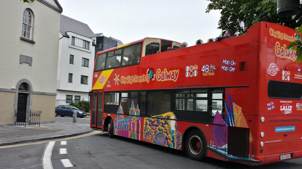 A red double-decker bus with "City Sightseeing Galway" signage and passengers on the upper deck drives through a street.