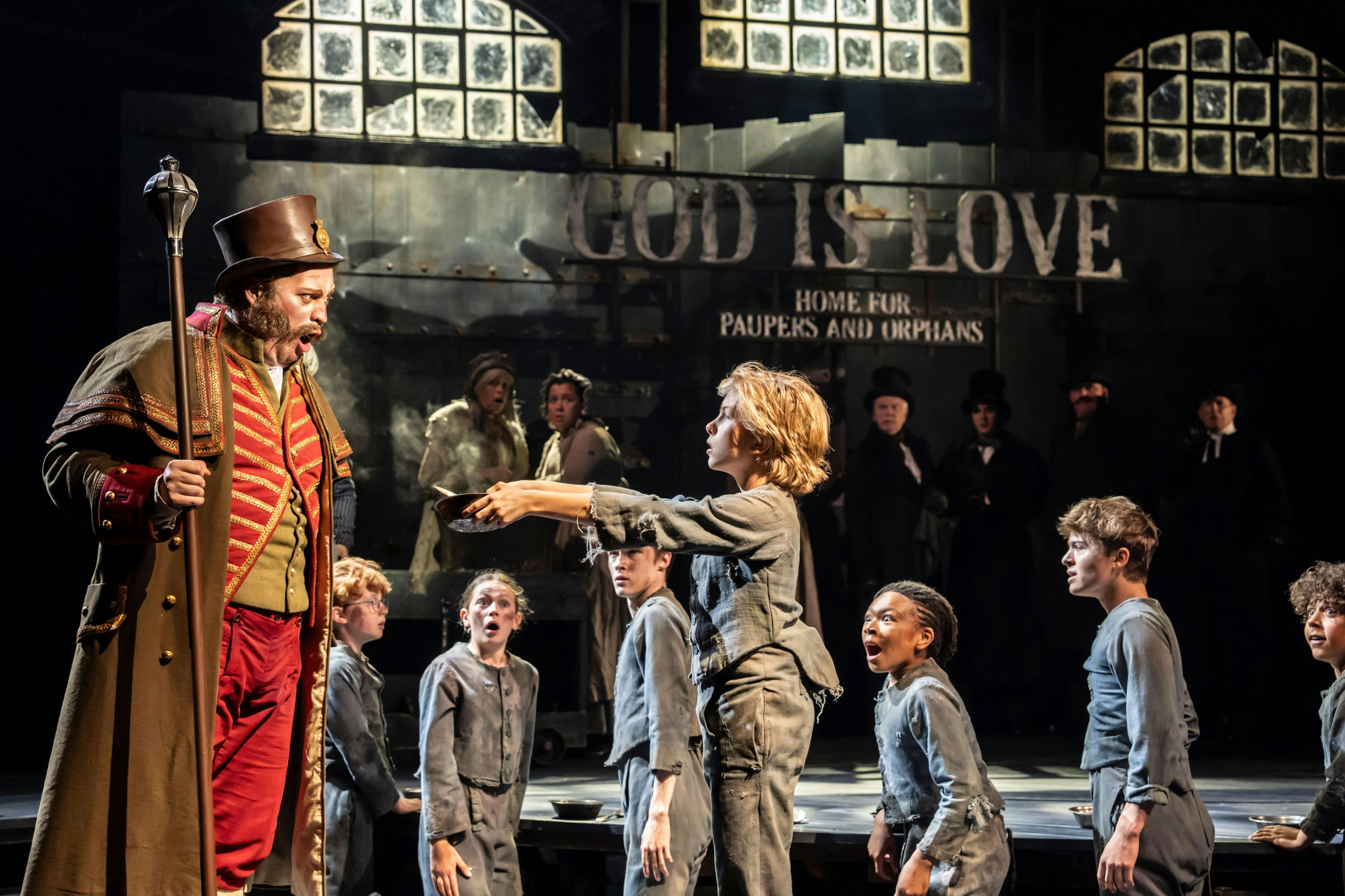 Un grup de nens amb roba andrajosa s'aixeca davant d'un cartell que diu "Déu és amor, la llar dels mendics i els orfes" amb els adults mirant.