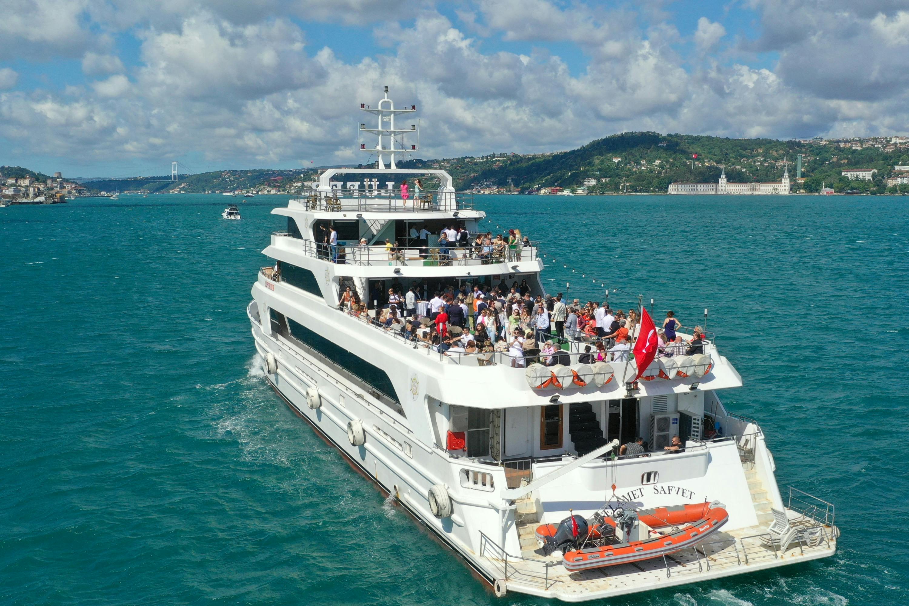 A white yacht with multiple decks filled with people, cruising on turquoise water near a distant coastline.
