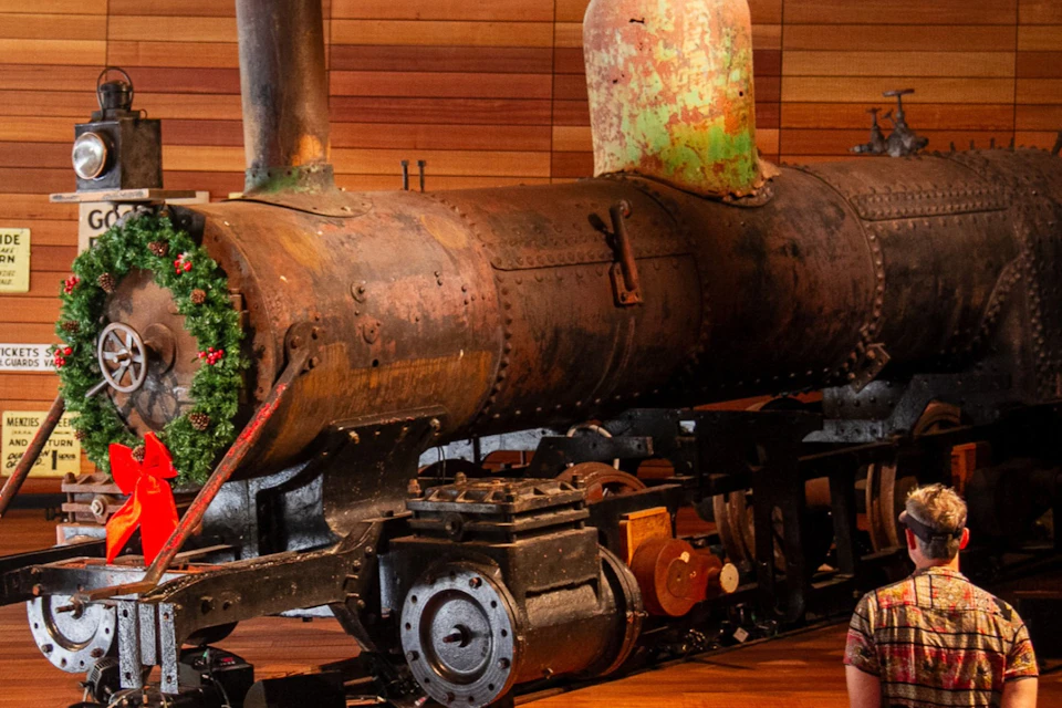 A vintage steam locomotive on display in a wooden-paneled room, adorned with a decorative wreath on the front.