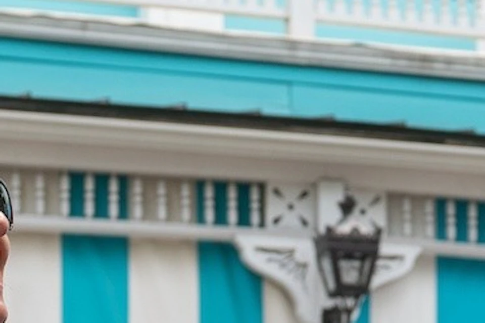 A tour guide in a blue shirt and hat speaking with two women in front of a turquoise and white striped building.