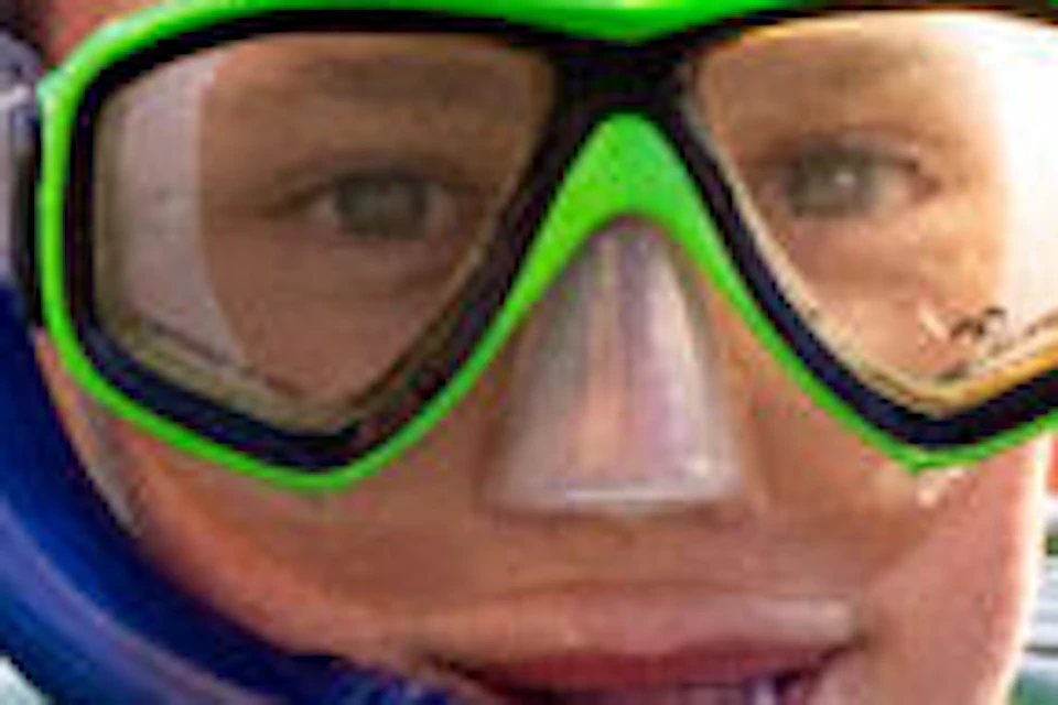 A person wearing a snorkel and mask gives a thumbs-up while floating in a clear body of water, with others snorkeling in the background.