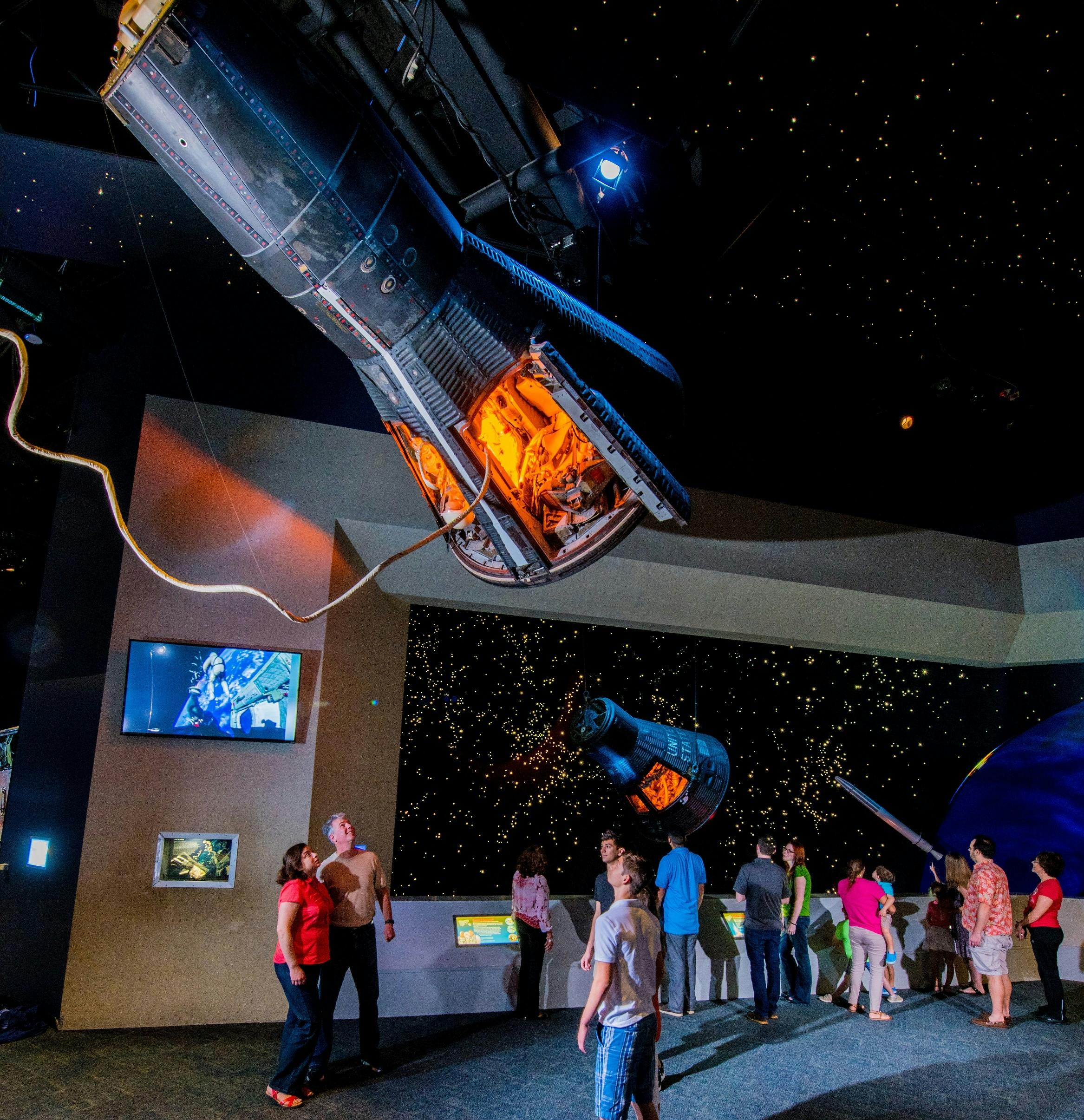 宇宙博物館で宇宙カプセルや星空の展示を見ている人たち。