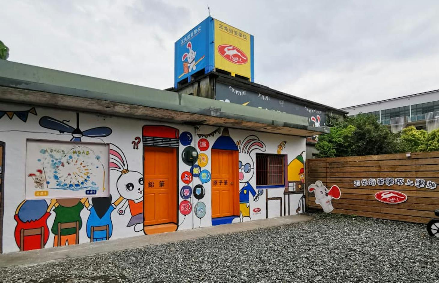 A building with colorful rabbit-themed murals, orange doors, and signs in Chinese text under a cloudy sky.