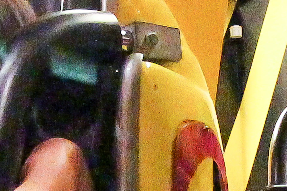 Two people, an adult and a child, sitting in yellow amusement ride seats with safety harnesses, surrounded by industrial decor.