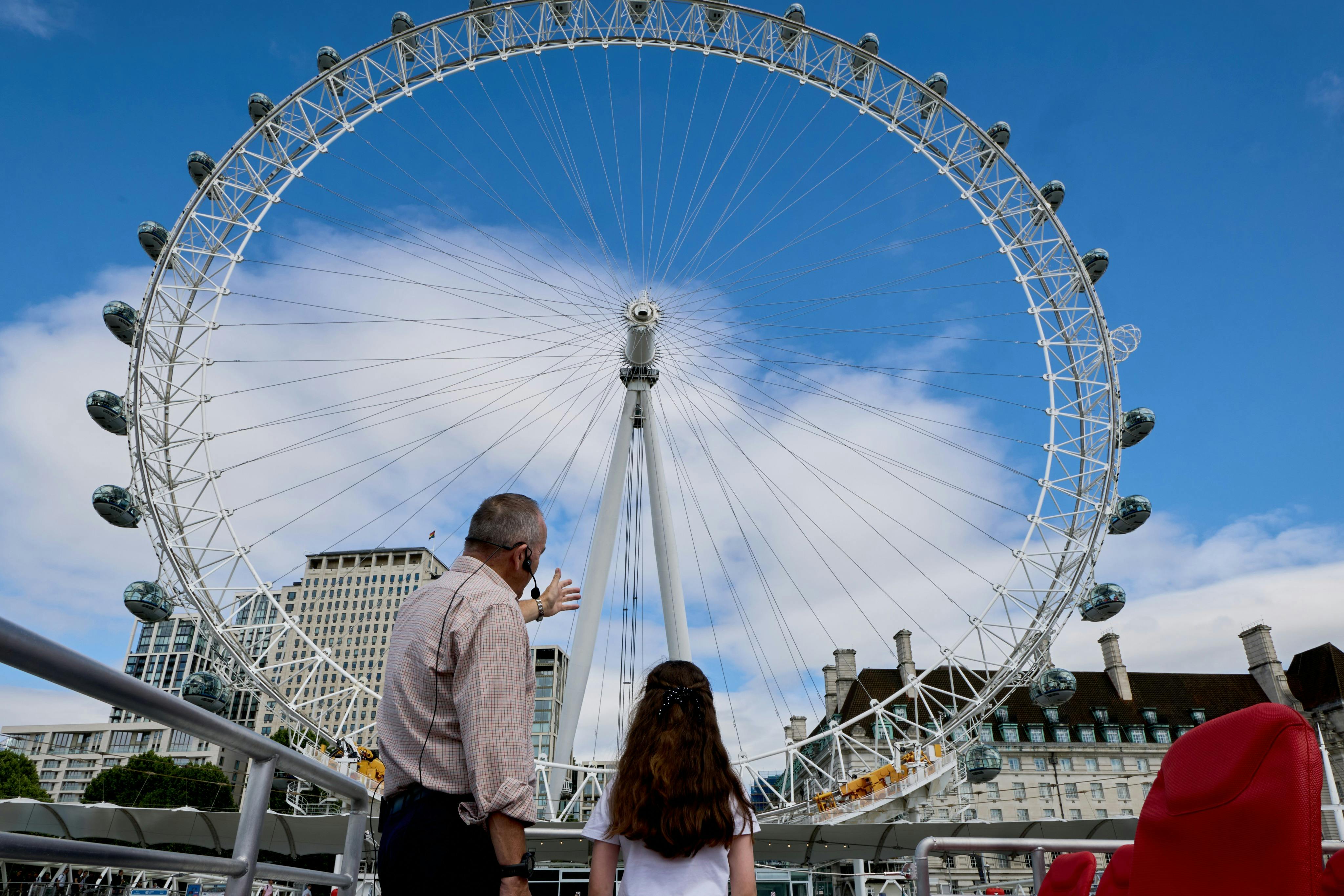 Un homme et une fillette lèvent les yeux vers une grande grande roue qui se détache sur un ciel bleu parsemé de nuages.